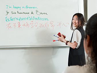 Eine Person schreibt in mehreren Sprachen ans Whiteboard.