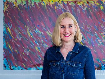 A blonde woman stands in front of a modern painting