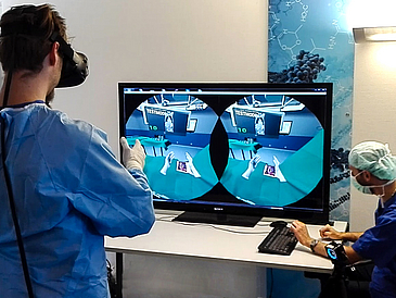 Zwei Ärzte vor einem Computerbildschirm, der einen virtuellen Operationssaal zeigt.