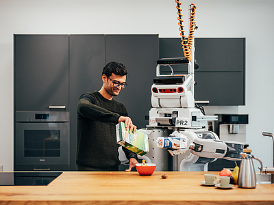 A robot and a person are standing in a kitchen.