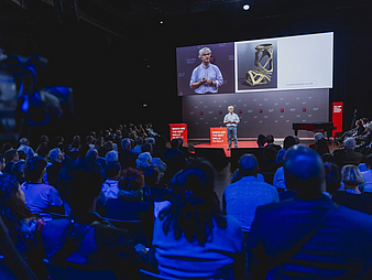 231109_FFW_PHT224.jpg Bild vom Falling Walls Science Summit: Person auf der Bühne mit großen Bildschirmen, davor Publikum