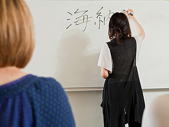 Eine Person schreibt in einer Fremdsprache ans Whiteboard.