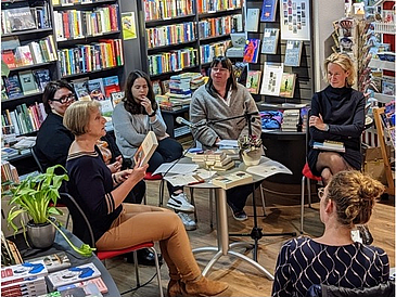 Menschen um einen Tisch sitzend in einer Buchhandlung vor Regalen