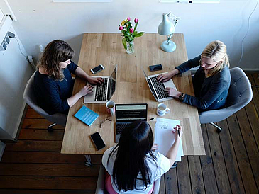 Drei Frauen sitzen mit jeweils einem Notebook an einem Tisch.