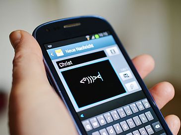 Smartphone mit Piktogramm eines Fisches und "Christ" im Absendertext einer Nachricht