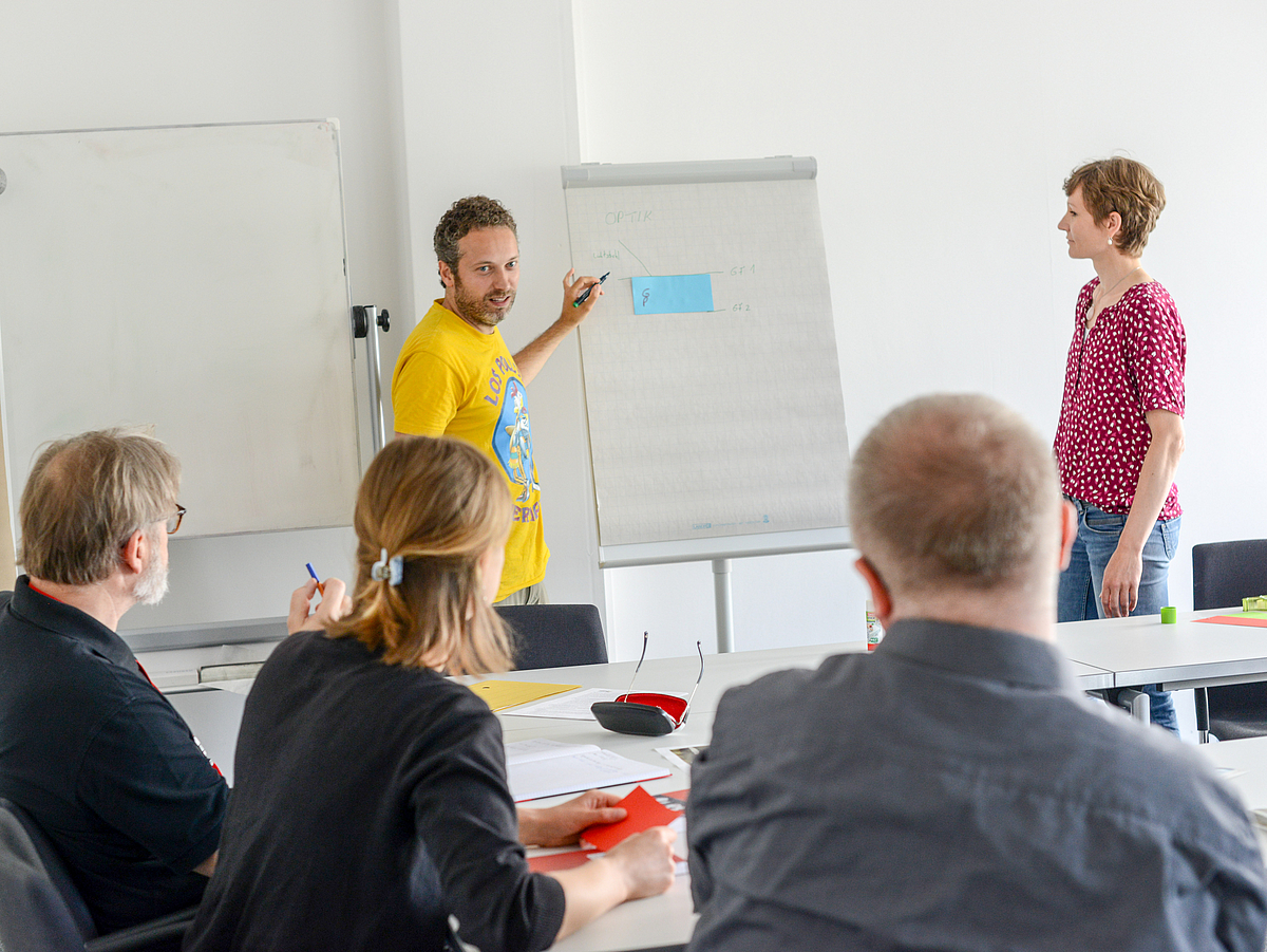 Zwei Lehrende arbeiten vor Zuhörern an einem Flipchart.