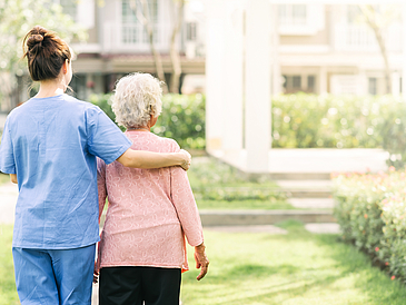 Pflegerin hilft einer Seniorin beim Spaziergang