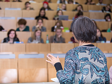 Eine Lehrende spricht vor Zuhörern im vollen Hörsaal.