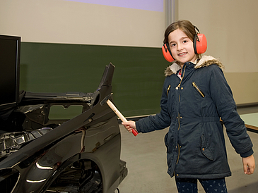 Kind mit Ohrenschützern haut mit Hammer auf schwarzes Metall. 