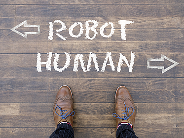 Man looking down at the words "Robot" and "Human" chalked onto the floor Ein Mann schaut auf die Wörter "Robot" und "Human" herab, die mit Kreide auf den Boden geschrieben wurden