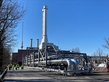 Man sieht eine Geothermieanlage mit vielen Rohren und einem weißen hohen Schornstein.