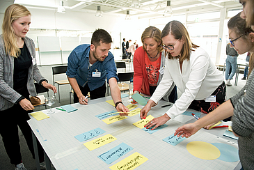 Studierende und ihre Mentorinnen stehen an einem Tisch