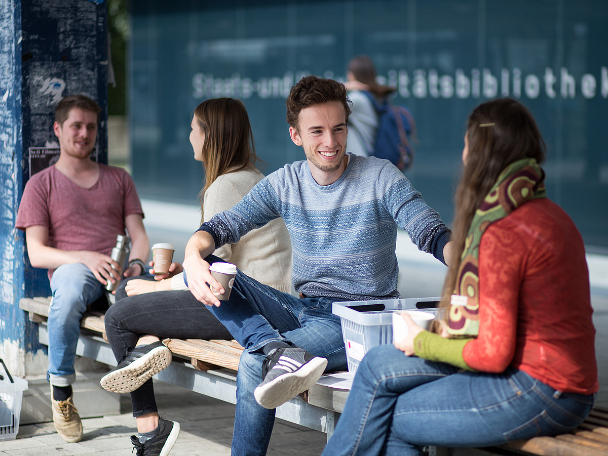 Studierende sitzen vor dem Eingang der Bibliothek.