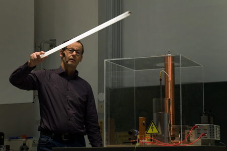 Prof. Nothold hält eine Leuchtstoffröre in die Nähe einer eingeschalteten Teslaspule und bringt die Leuchtstoffröhre amit zum Leuchten.