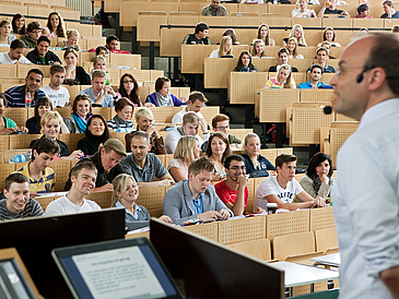 Studierende in einem Hörsaal, Professor im Vordergrund