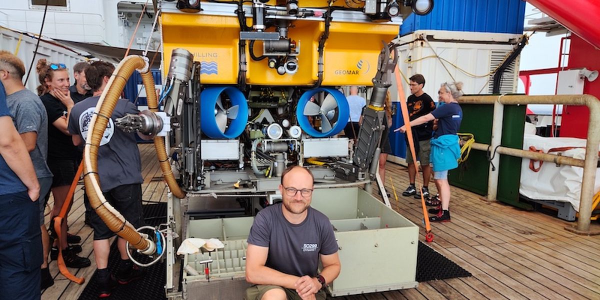 Several scientists stand in front of and next to the yellow remote-controlled underwater vehicle Kiel 6000 on the deck of the research vessel Sonne.
