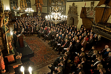 Menschen sitzen in einem festlichen Saal und hören einer Vortragenden zu.