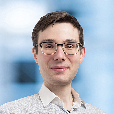 Person mit braunes Haar, Brille und weißem Hemd lacht