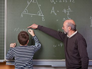 Mathelehrer mit Schüler an einer Tafel