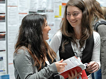 Zwei junge Frauen unterhalten sich auf einer Messe.