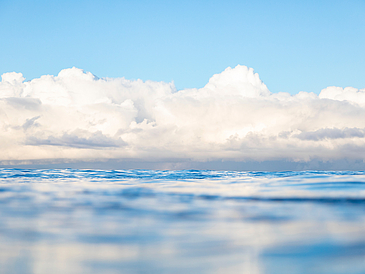 Weiße Wolken am Himmel über einer blauen Wasserfläche