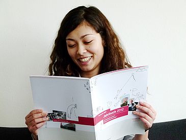 Junge Frau liest lächelnd in einer Publikation.