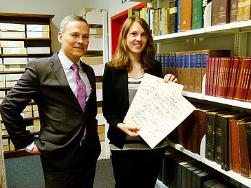 Ein Mann und eine Frau in einer Bibliothek, die Frau hält alte Notenblätter in den Händen.