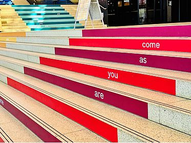 Bunte Stufen mit Aufschrift "Come As You Are" im Eingang Zentralbereich der Uni Bremen in der Glashalle
