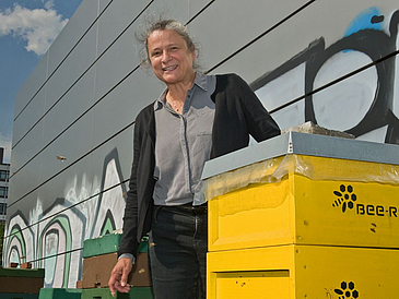 Frau steht zwischen Bienenkörben