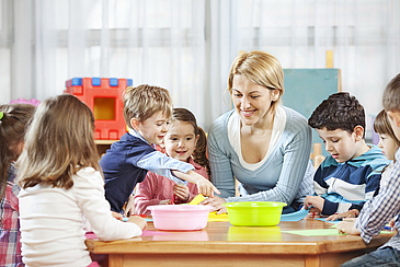  Lehrerin arbeitet mit Kindern am Tisch. 