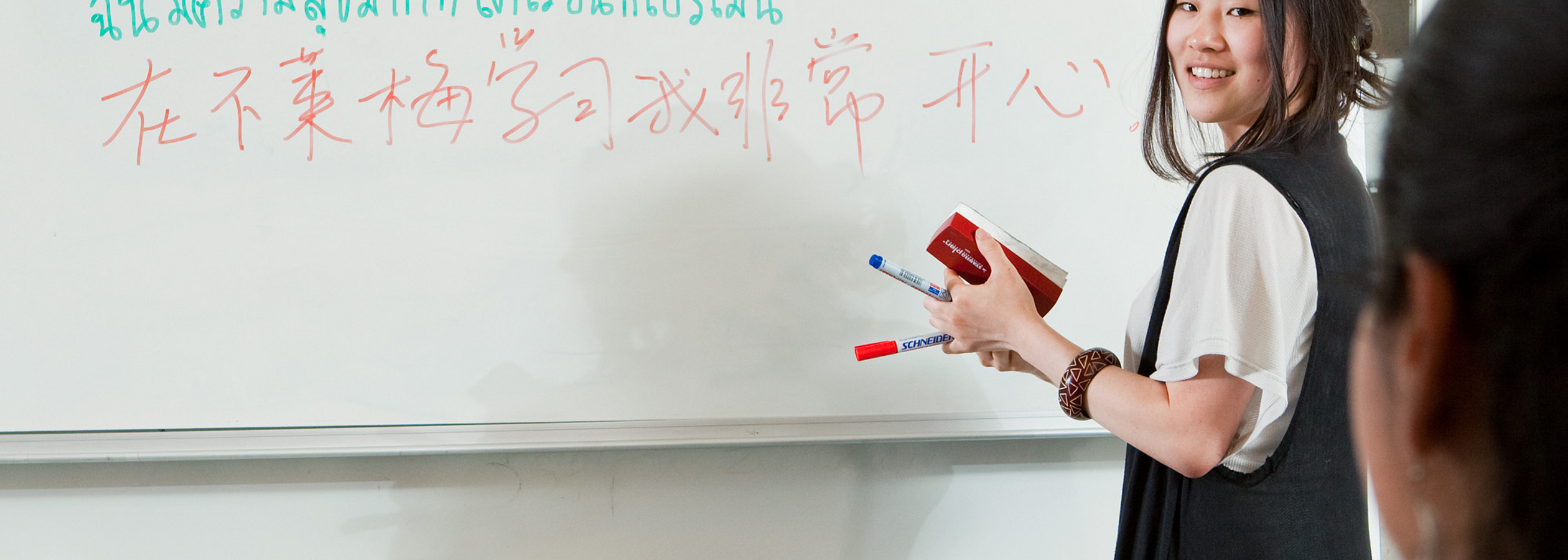 A person writes in different languages on a whiteboard.