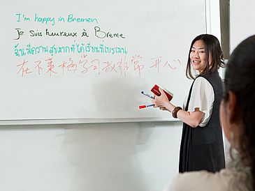 Eine Person schreibt in mehreren Sprachen ans Whiteboard.