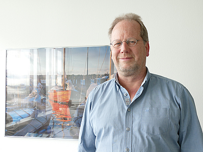 Portrait von Andree Hagedorn vor einem an der Wand hängenden Bild.