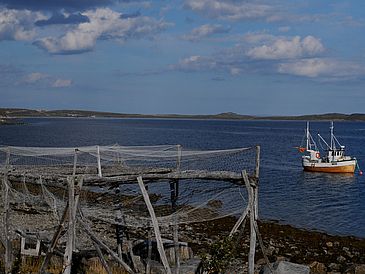 Fjord mit Fischerboot, im Vordergrund sind Fischernetze aufgehängt.