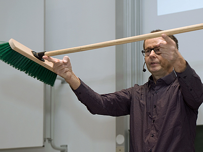 Prof. Nothold erklärt anhand eines auf den beiden Zeigefingern balancierten Besens, wo dieser seinen Schwerpunkt hat.