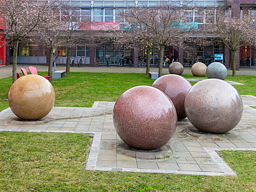 Large granite stone balls are scattered on a green area in front of a building