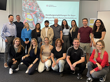 Gruppenfoto Bayer04 Es sind mehrere Personen vor einem Beamerprojektion zu sehen