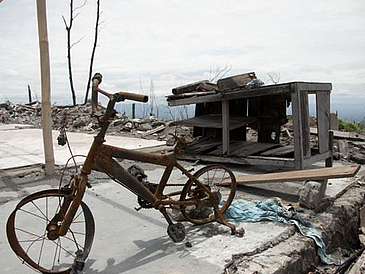 Die Überreste eines vebrannten Kinderfahrrads stehen vor einer ebenfalls verbrannten Landschaft
