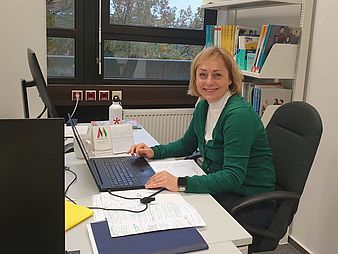 Prof. Sylwia Adamczak-Krysztofowicz sitzt im Büro und arbeitet, dabei lächelt sie in die Kamera