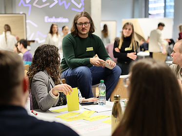 Wirtschaftspsychologie Studiengang Mehrere Studenten um einen Tisch eine Studentin hält eine gelben Klebezettel.
