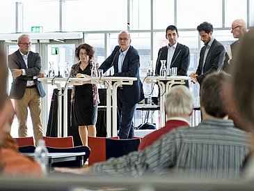 Podium mit sechs Personen, fünf Männer, eine Frau