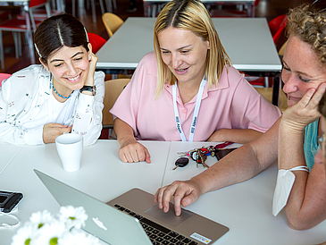 Drei Frauen schauen auf einen Laptop.