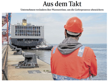 Person mit rotem Helm und roter Jacke steht im Vordergrund auf einem Schiff.