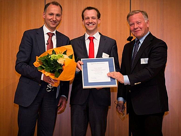 Gruppenbild mit drei Männern mit Urkunde und Blumenstrauß