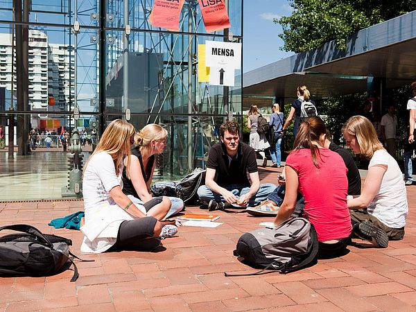 Studierende sitzen vor der Glashalle.