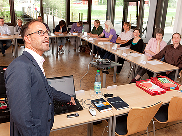 Ein Lehrender vor einer Gruppe Zuhörer in einem Seminarraum.