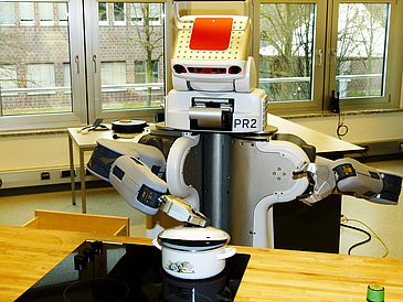 Roboter kippt Popcorn aus Kochtopf in Schüssel.