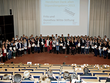 Gruppenbild mit mehr als 100 Studierenden auf einer Art Theaterbühne.