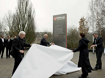 Drei Männer und eine Frau enthüllen eine Stele.