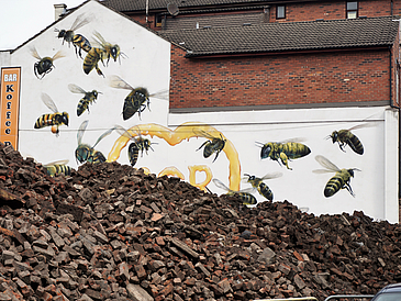 Hinter einem Schutthaufen ist eine Schutthaufen zu sehen mit Graffiti in Form großer gelb-schwarzer Bienen